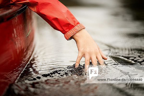Cropped hand of girl touching water while traveling in boat on river