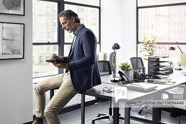 Geschäftsmann benutzt Tablet-Computer  während er im Büro am Schreibtisch sitzt