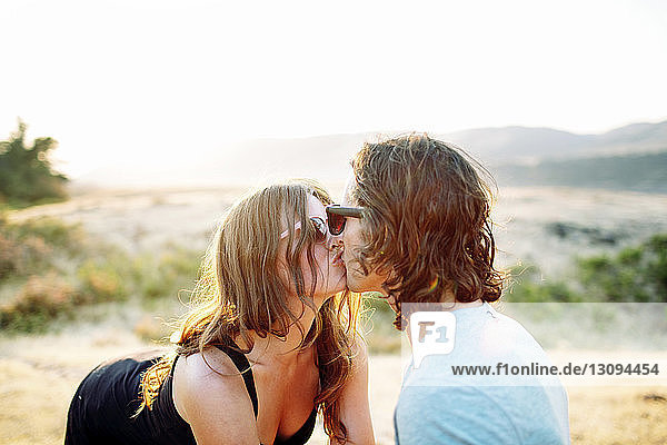 Glückliches Paar küsst sich auf dem Feld vor klarem Himmel