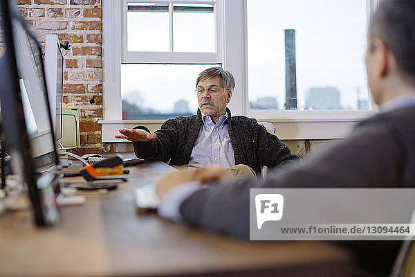 Businessmen discussing while sitting at desk by window in office