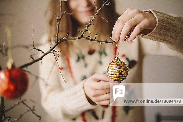 Midsection of woman hanging bauble on twig during Christmas at home