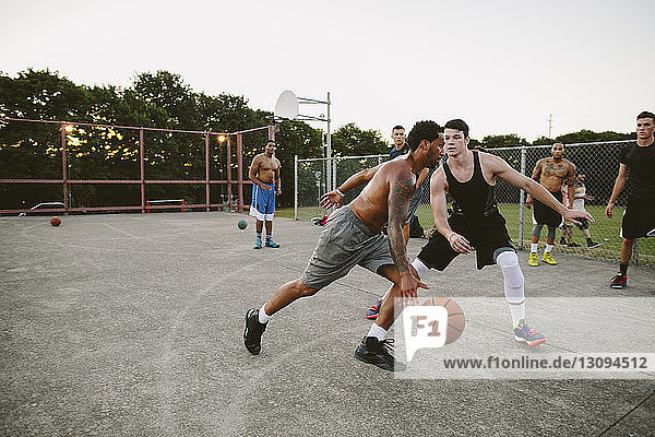 Männliche Freunde spielen Basketball auf dem Platz gegen den klaren Himmel