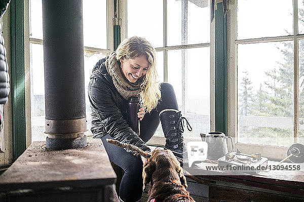 Happy woman playing with dog in cottage