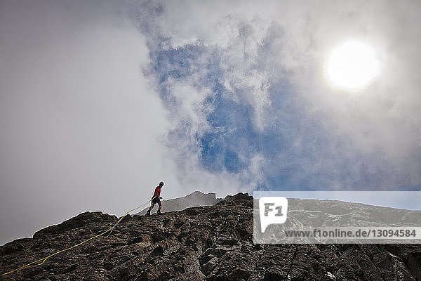 Tiefwinkelansicht eines Wanderers  der an Felsformationen vor bewölktem Himmel klettert