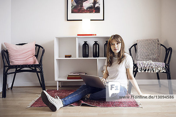 Porträt einer jungen Frau  die zu Hause mit Laptop auf dem Boden sitzt