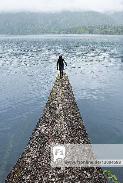 Woman in warm clothing walking on pier over lake in forest
