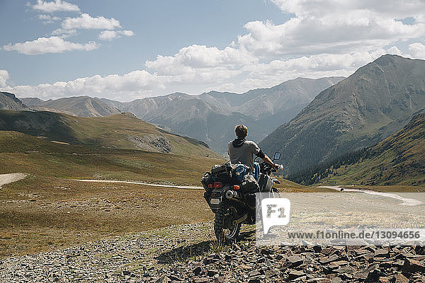 Rear view of biker riding motorbike on mountain against cloudy sky