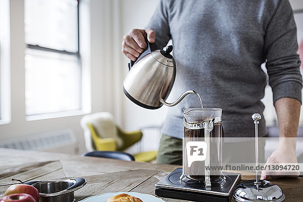 Ein Mann gießt Wasser in die französische Presse  während er zu Hause Kaffee kocht