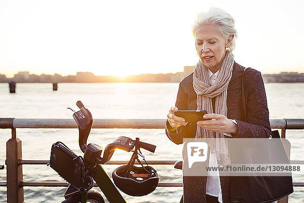 Ältere Frau benutzt Smartphone mit dem Fahrrad gegen das Meer