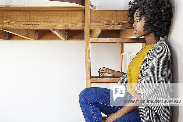 Side view of woman looking away while sitting on bunkbed ladder