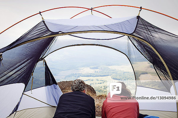 Rear view of couple relaxing in tent at campsite