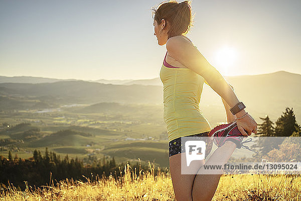 Side view of woman exercising on mountain against clear sky during sunny day