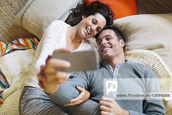 Overhead view of couple taking selfie while lying on carpet at home