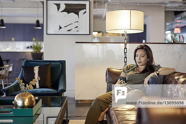 Geschäftsfrau benutzt Smartphone  während sie im Kreativbüro auf dem Sofa sitzt