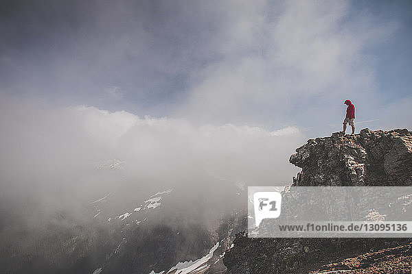 Side view of hiker standing on cliff against cloudy sky