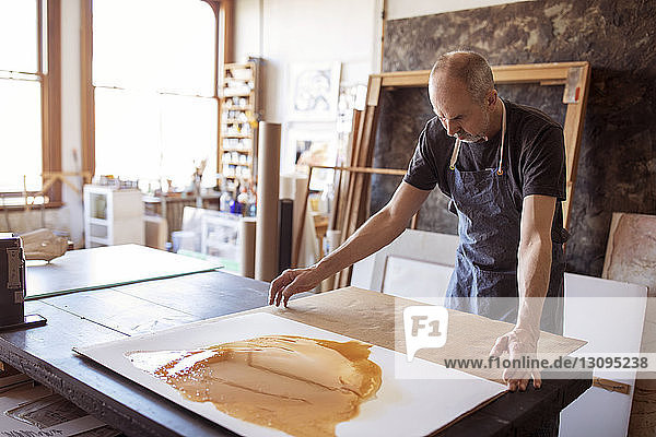 Senior artist making paintings at table in workshop