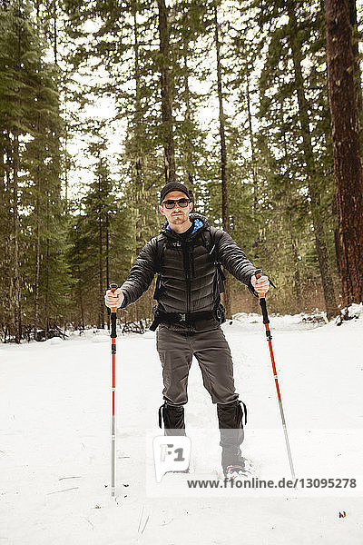 Portrait of man wearing sunglasses hiking in snow covered forest