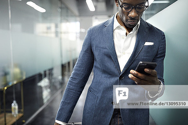 Seriöser Geschäftsmann benutzt Smartphone  während er im Büro steht