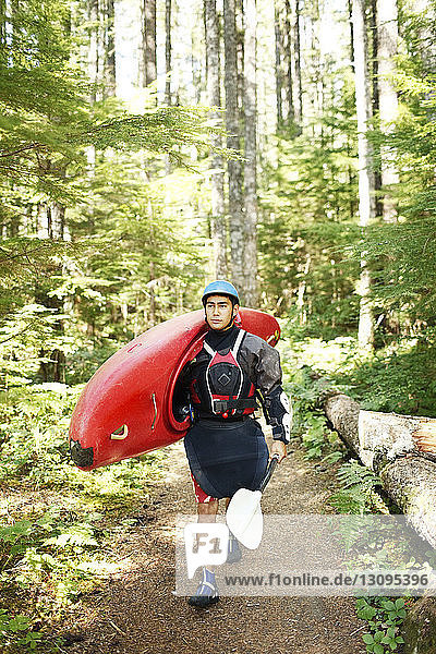 Young man carrying kayak while walking in forest