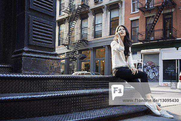 Junge Frau  die auf einer Treppe im Freien sitzend ein Smartphone beantwortet