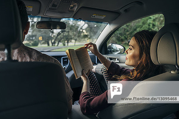 Ehefrau liest Buch  während sie mit ihrem Mann im Auto unterwegs ist