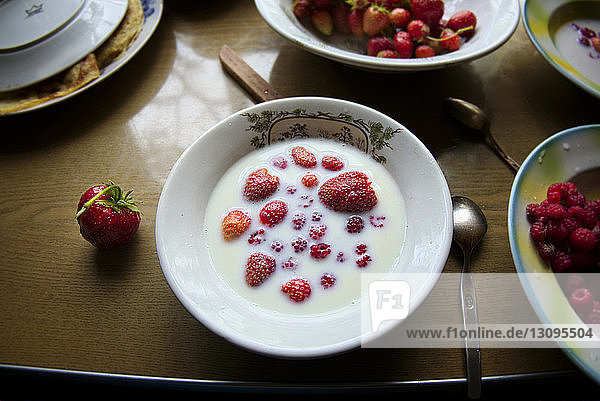 Hochwinkelansicht von Erdbeeren und Milch in Schale auf Holztisch