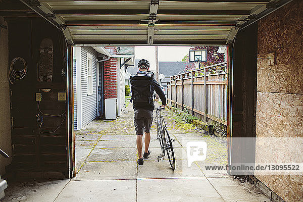 Rückansicht eines männlichen Pendlers mit Fahrrad auf dem Fußweg durch die Garage gesehen