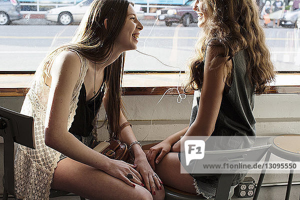 Lächelnde Freundinnen hören Musik  während sie im Café sitzen