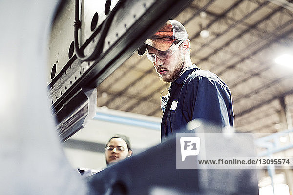 Serious man working with coworker by machinery in industry