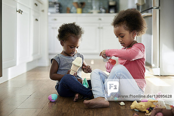Schwestern spielen mit Eisspielzeug  während sie zu Hause auf dem Hartholzboden sitzen