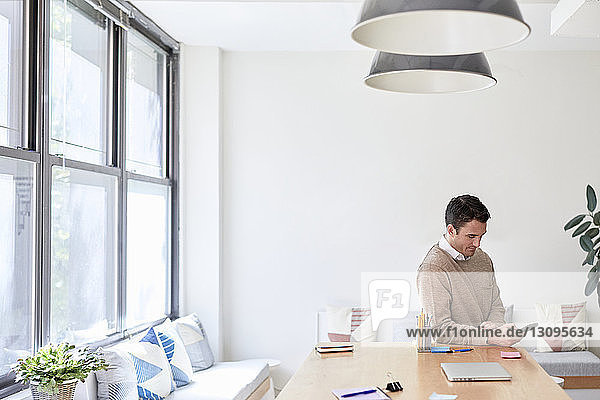 Businessman using mobile phone while sitting at table against wall in creative office