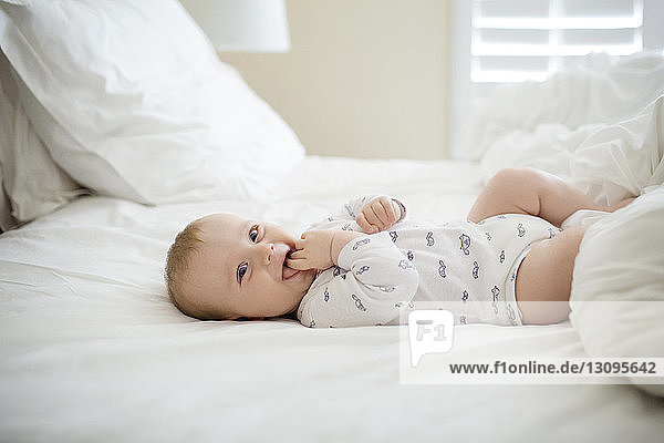Cheerful baby boy lying on bed at home