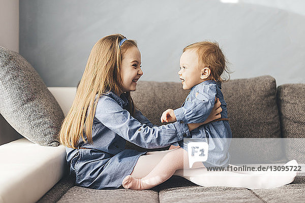 Seitenansicht eines glücklichen Mädchens das mit seiner Schwester spielt während es zu Hause auf dem Bett sitzt