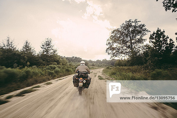 Rückansicht eines Motorradfahrers mit Sturzhelm beim Motorradfahren auf unbefestigter Straße gegen den Himmel