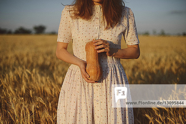 Mittelsektion einer Frau in einem Kleid  die Kürbis hält  während sie bei Sonnenuntergang auf einem Bauernhof steht