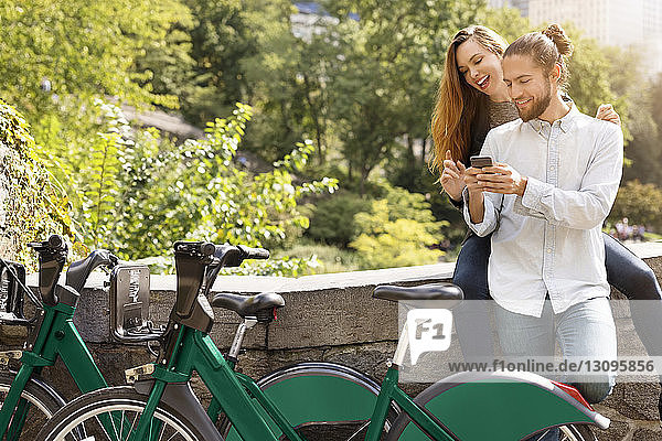 Couple using mobile phone while leaning on retaining wall