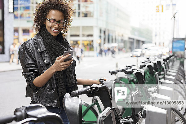 Glückliche Frau benutzt Mobiltelefon  während sie am Fahrradträger steht
