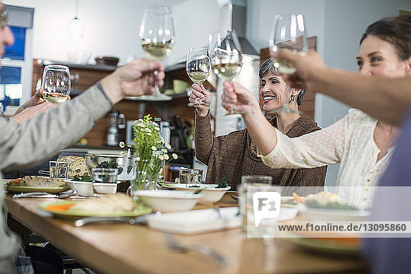 Happy friends toasting wine while sitting at table during social gathering
