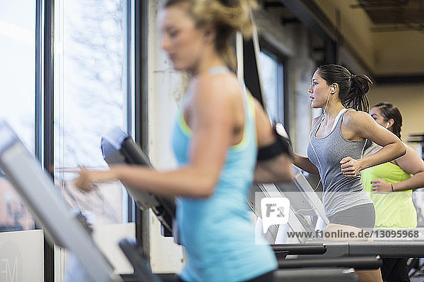 Frauen  die Musik hören  während sie im Fitnessstudio auf Laufbändern trainieren