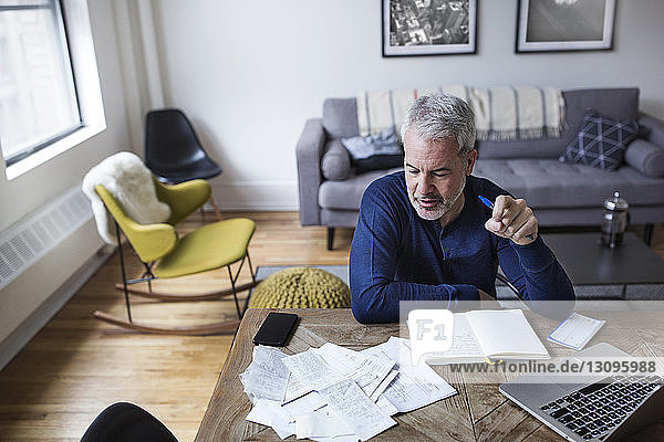 High angle view of mature man analyzing bills at table in home