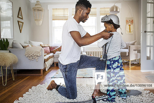 Father putting suit of armor on boy at home