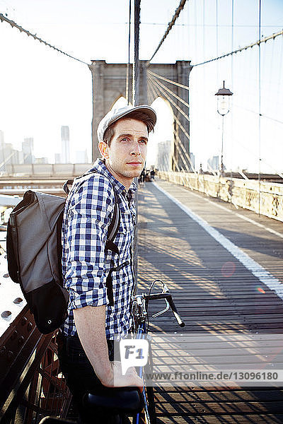 Thoughtful man holding bicycle and standing on Brooklyn Bridge