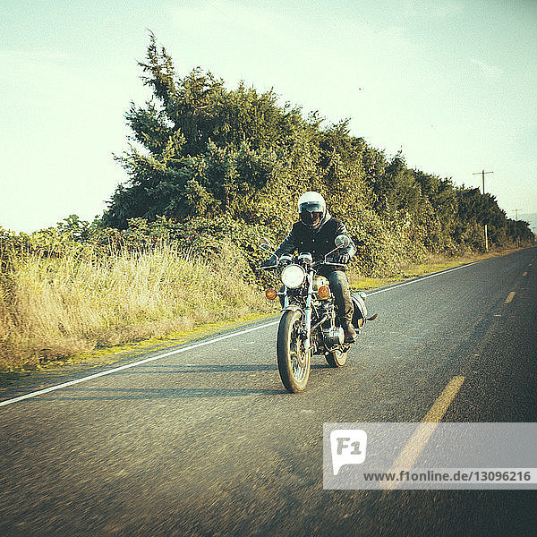 Male biker riding motorcycle on country road against sky