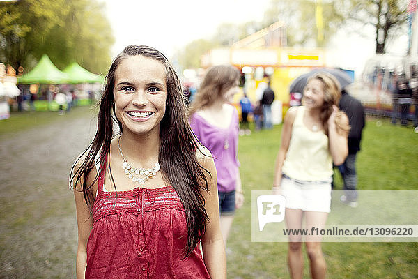Portrait of happy woman standing with friends in background at amusement park