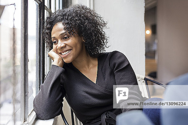 Smiling thoughtful businesswoman sitting by windows at office