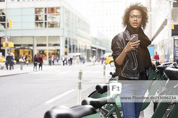 Woman using mobile phone while standing by bicycles at parking lot