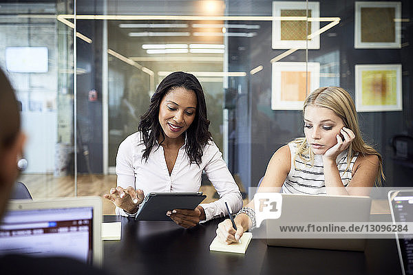 Businesswomen using technologies while sitting in meeting at conference table