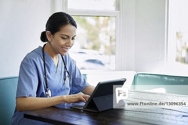 Lächelnde Ärztin mit Tablet-Computer bei Tisch im Krankenhaus