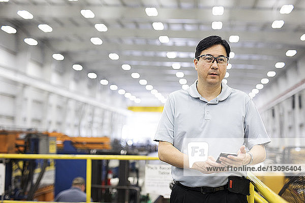 Vorgesetzter mit Smartphone in der Hand  während er in einer Fabrik der Stahlindustrie steht