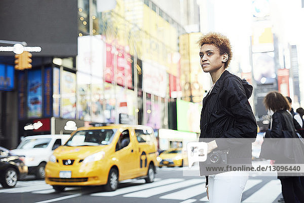 Seitenansicht einer jungen Frau mit Digitalkamera  die auf der Straße der Stadt steht